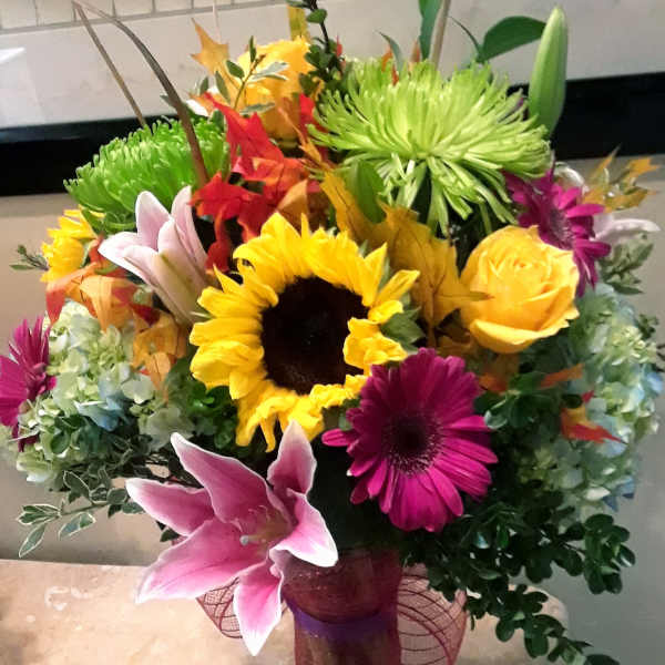 Colorful mixed bouquet in a glass vase with sunflowers, lilies, and chrysanthemums