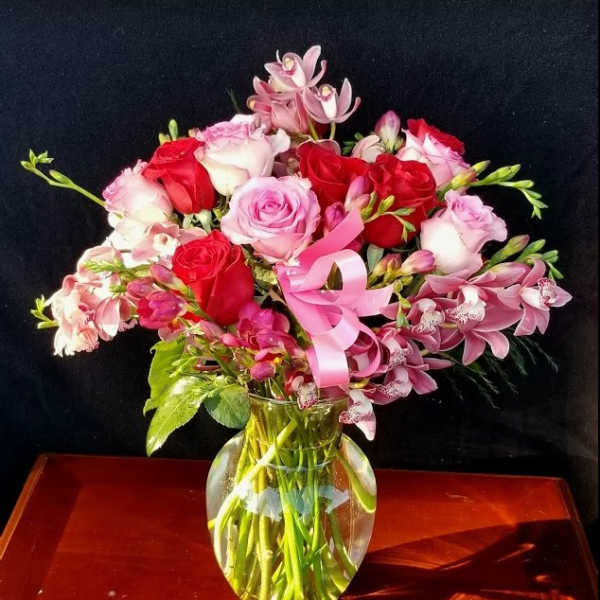 Pink and red roses with orchids in a glass vase