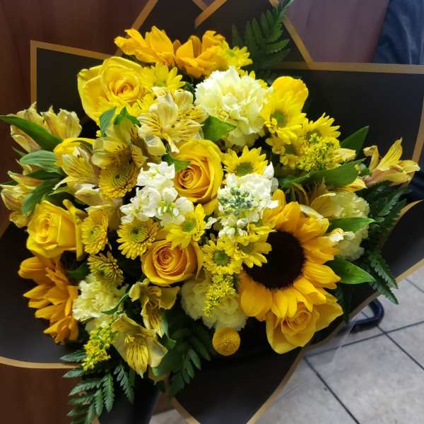 Yellow bouquet with roses, sunflowers, and white blooms wrapped in black paper