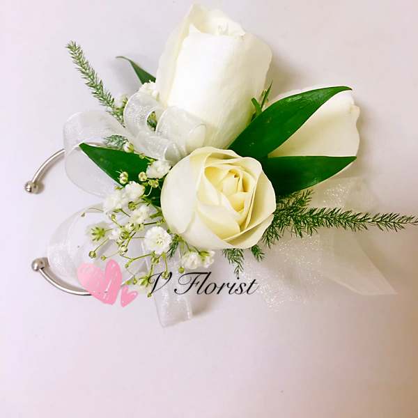 White rose wrist corsage with small white filler flowers and sheer ribbon on a silver cuff.
