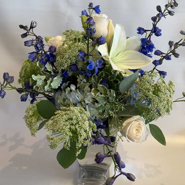 White roses and blue flowers in a clear glass vase