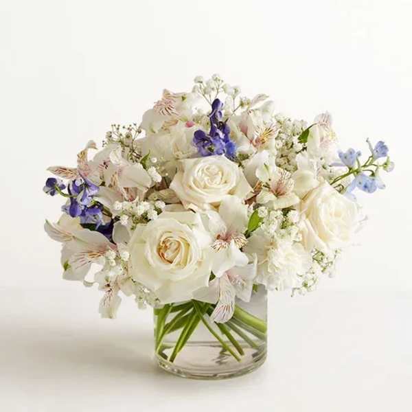 White rose bouquet with purple and pale blue flowers in a clear glass vase