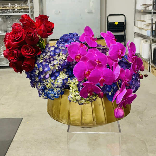 Red roses, blue hydrangeas, and pink orchids arranged in a gold bowl
