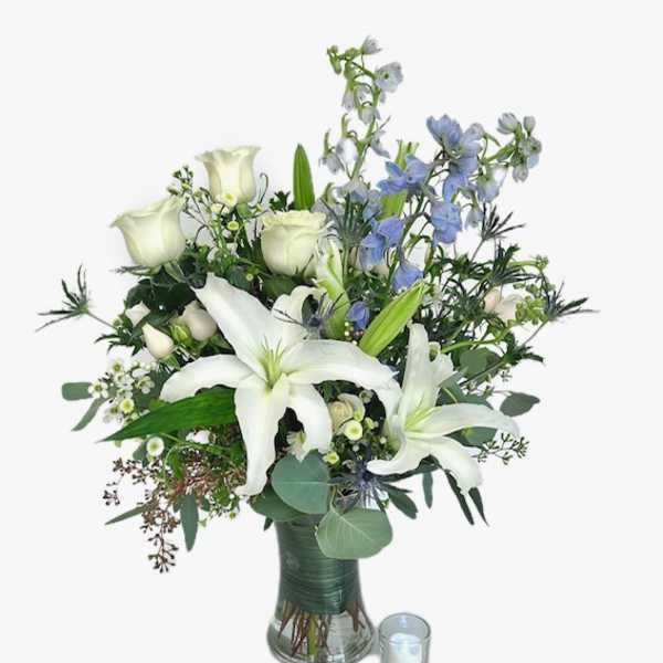 White lilies and roses in a glass vase with a small candle beside it