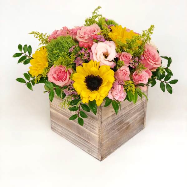 Low wooden box arrangement with yellow sunflowers and pink roses accented by green and purple blooms