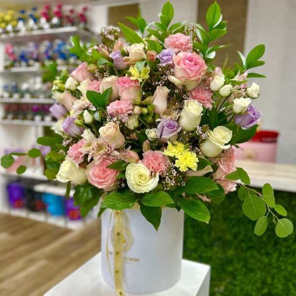 Pastel arrangement of roses, carnations, and mums in a white hat box-style container.