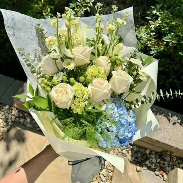Bouquet of white roses, blue hydrangea, and green accents wrapped in paper