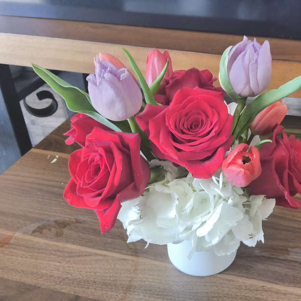Short arrangement of red roses, tulips, and white hydrangeas in a white vase