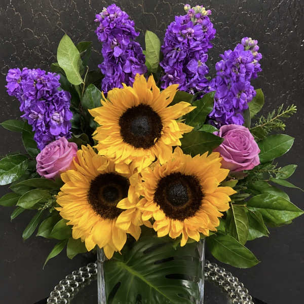Sunflowers, purple stock, and pink roses in a clear glass vase