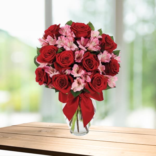 Red roses and pink alstroemeria in a clear glass vase with a red bow