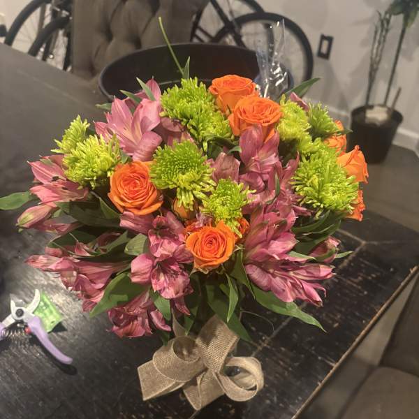Bouquet of orange roses, pink alstroemeria, and green chrysanthemums tied with burlap ribbon
