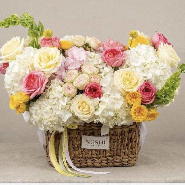 Basket arrangement of white and pink roses with yellow accents