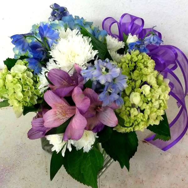 Bouquet of blue, pink, white, and green flowers with a purple ribbon