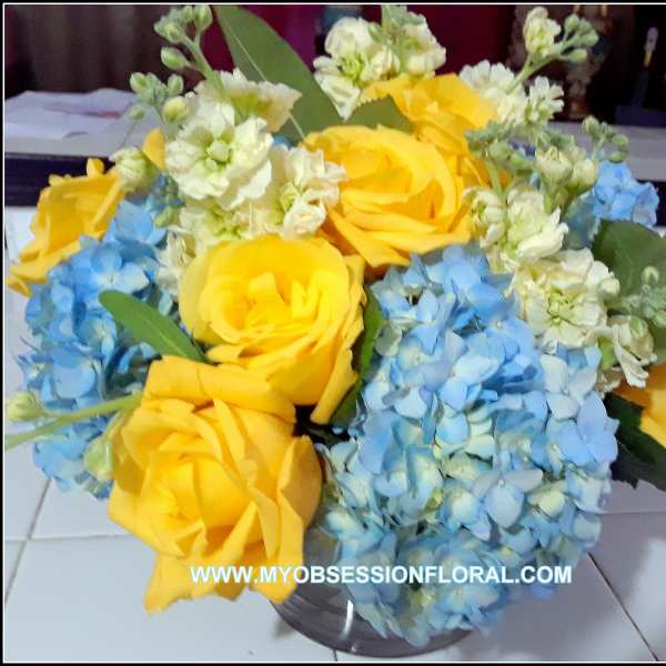 Bouquet of yellow roses and blue hydrangeas in a clear vase