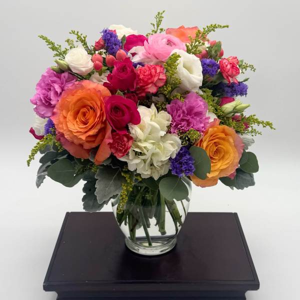 Bright mixed bouquet of roses, carnations, and hydrangeas in a round clear glass vase