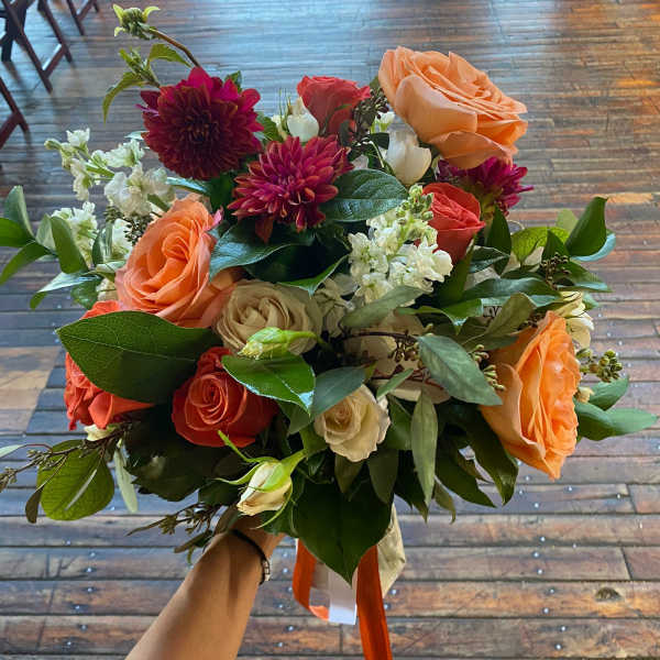 Handheld bouquet of peach and coral roses with burgundy blooms