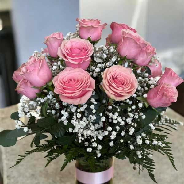 Pink roses and baby's breath in a glass vase with a pink ribbon