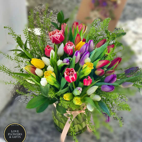 Mixed tulip bouquet in a glass vase with a pink ribbon