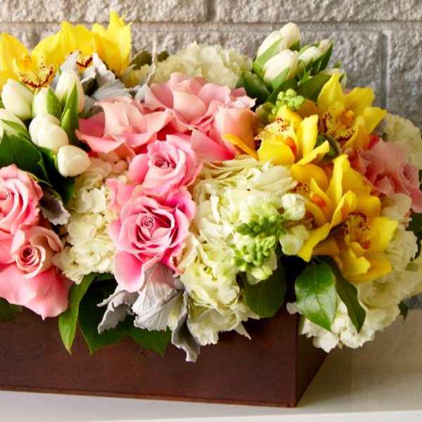 Pink roses and yellow orchids arranged in a rectangular box with white blooms