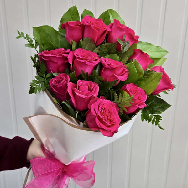 Bouquet of bright pink roses wrapped in white paper with a pink ribbon