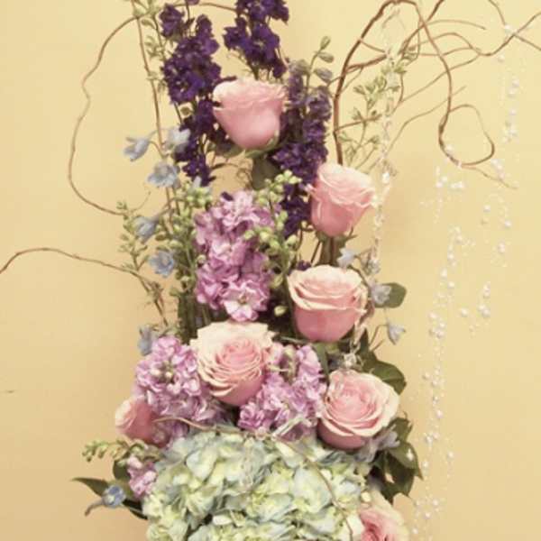 Tall floral arrangement with pink roses, hydrangea, and purple blooms in a silver vase