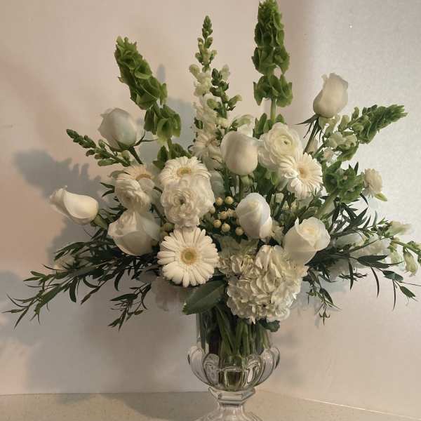 White floral arrangement in a clear glass vase with tall green spikes
