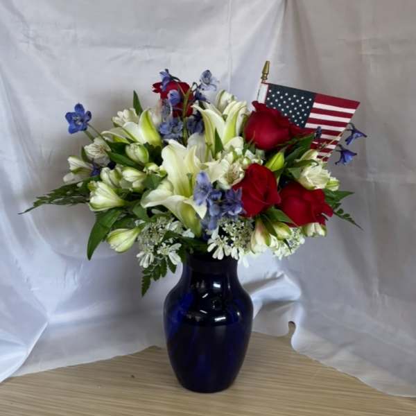 Bouquet of red roses, white lilies, and blue flowers in a dark vase with an American flag