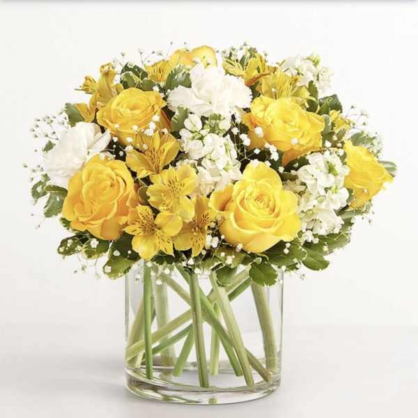 Yellow roses and white flowers arranged in a clear glass vase.