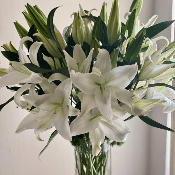 White lilies arranged in a tall clear glass vase