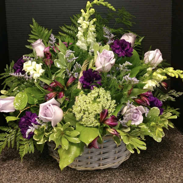 Basket arrangement of lavender roses, purple blooms, and white flowers