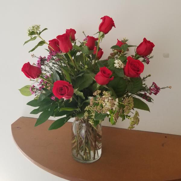 Arrangement of red roses with small white and pink filler flowers in a clear glass vase
