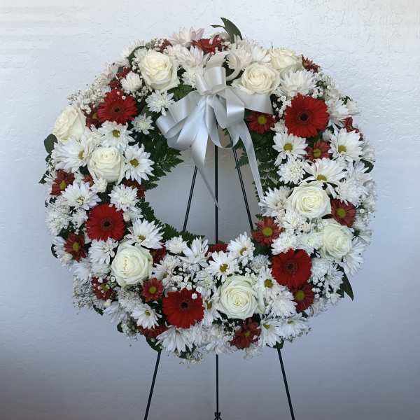 Circular wreath of white and red flowers on a stand with a white ribbon