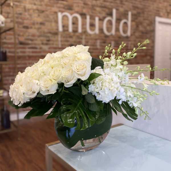 White roses and orchids in a round glass vase