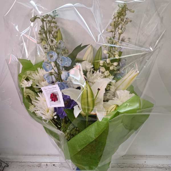 Wrapped bouquet of white, blue, and purple flowers with lilies and daisies