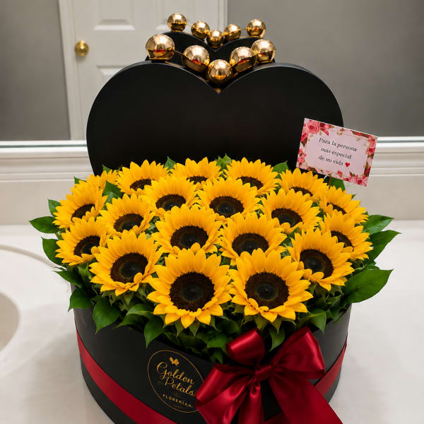 Heart-shaped box of yellow sunflowers with a red ribbon and gold topper