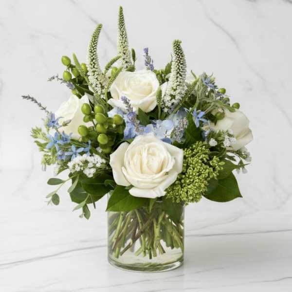 White roses and blue flowers arranged in a clear glass vase