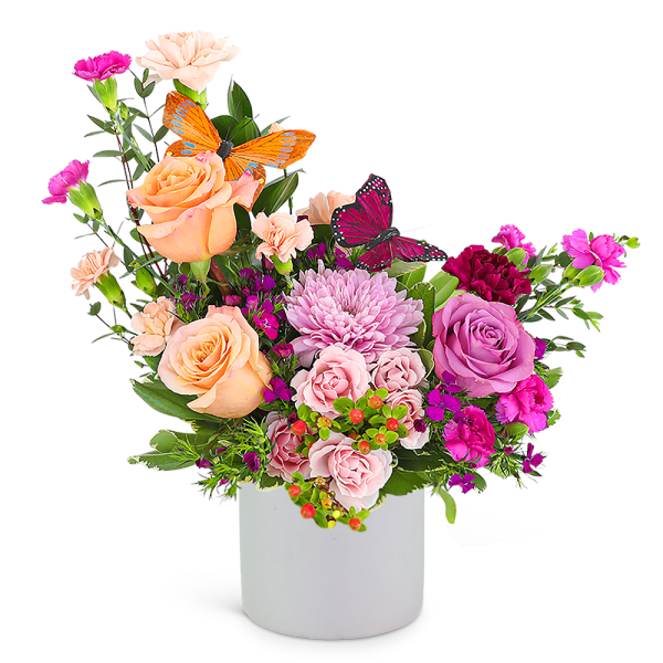 Mixed pink and peach flower arrangement in a white vase with butterfly picks