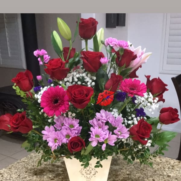 Mixed bouquet of red roses, pink daisies, and lilies in a white vase