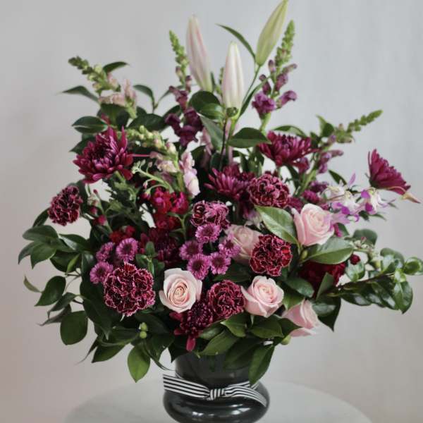 Pink and burgundy floral arrangement in a black vase