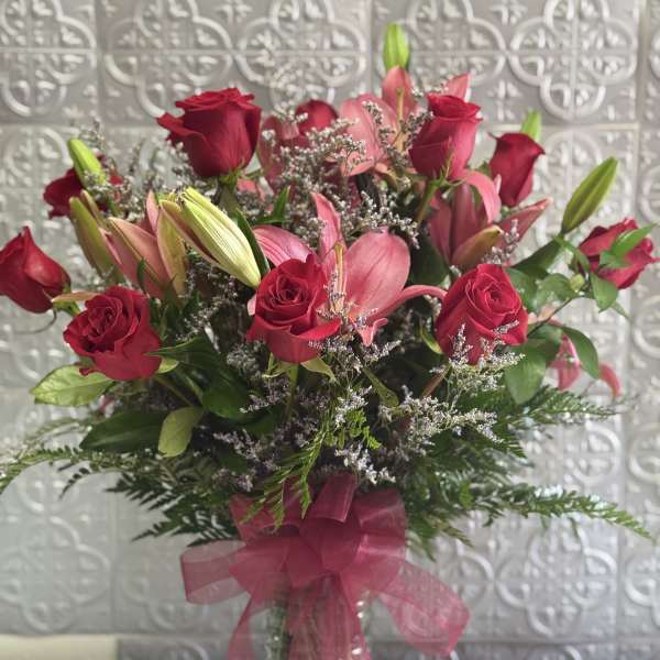 Bouquet of red roses and pink lilies in a clear glass vase with a pink ribbon