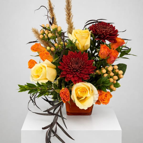 Arrangement of yellow and orange roses with red chrysanthemums in a square vase