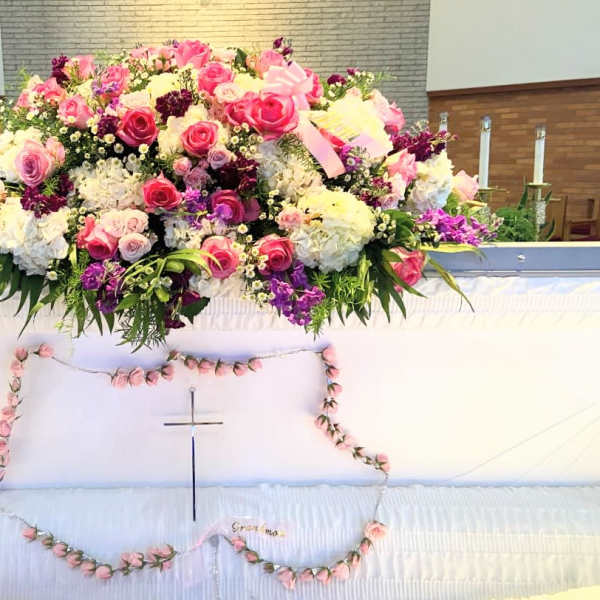 Large pink, white, and purple floral spray on a white casket