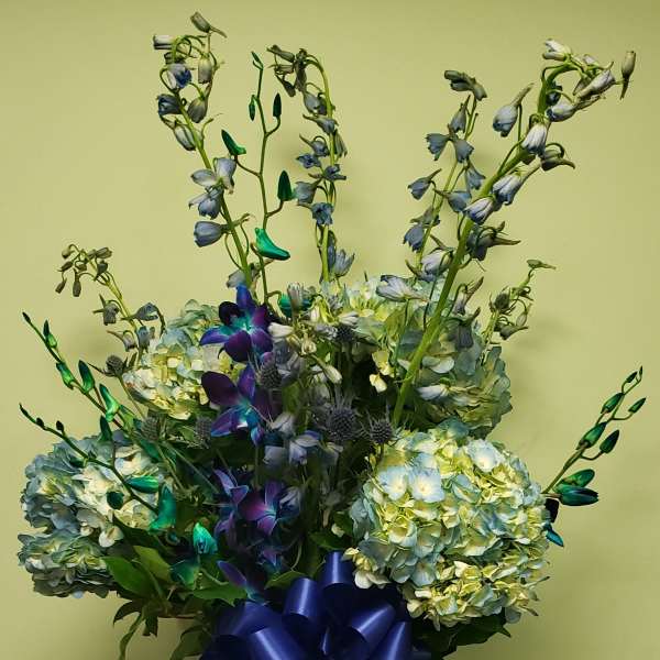 Blue hydrangea and orchid arrangement in a tall glass vase with a blue ribbon