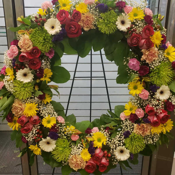 Large circular floral wreath with mixed roses, daisies, and mums