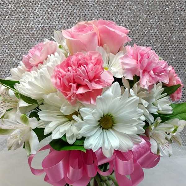 Pink roses and carnations with white daisies in a glass vase with a pink ribbon bow