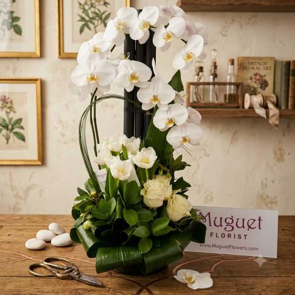 White orchids and roses arranged in a black vase with broad green leaves