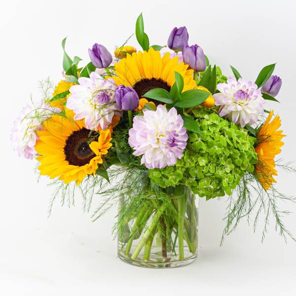 Sunflowers and purple blooms in a clear glass vase