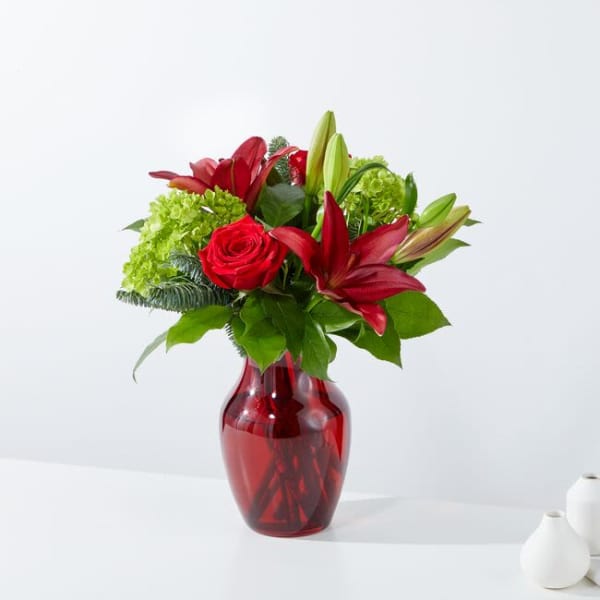 Red roses and lilies arranged in a red glass vase