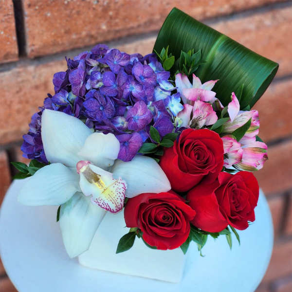 Bouquet of red roses, purple hydrangea, and white orchids in a white box