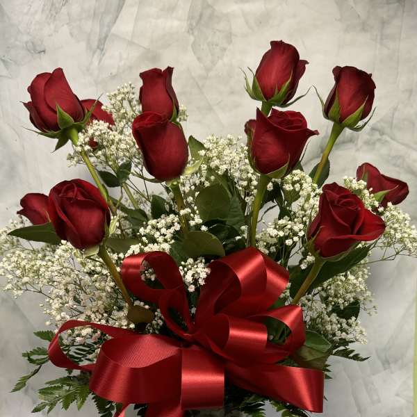 Red roses in a clear glass vase with baby's breath and a red ribbon bow